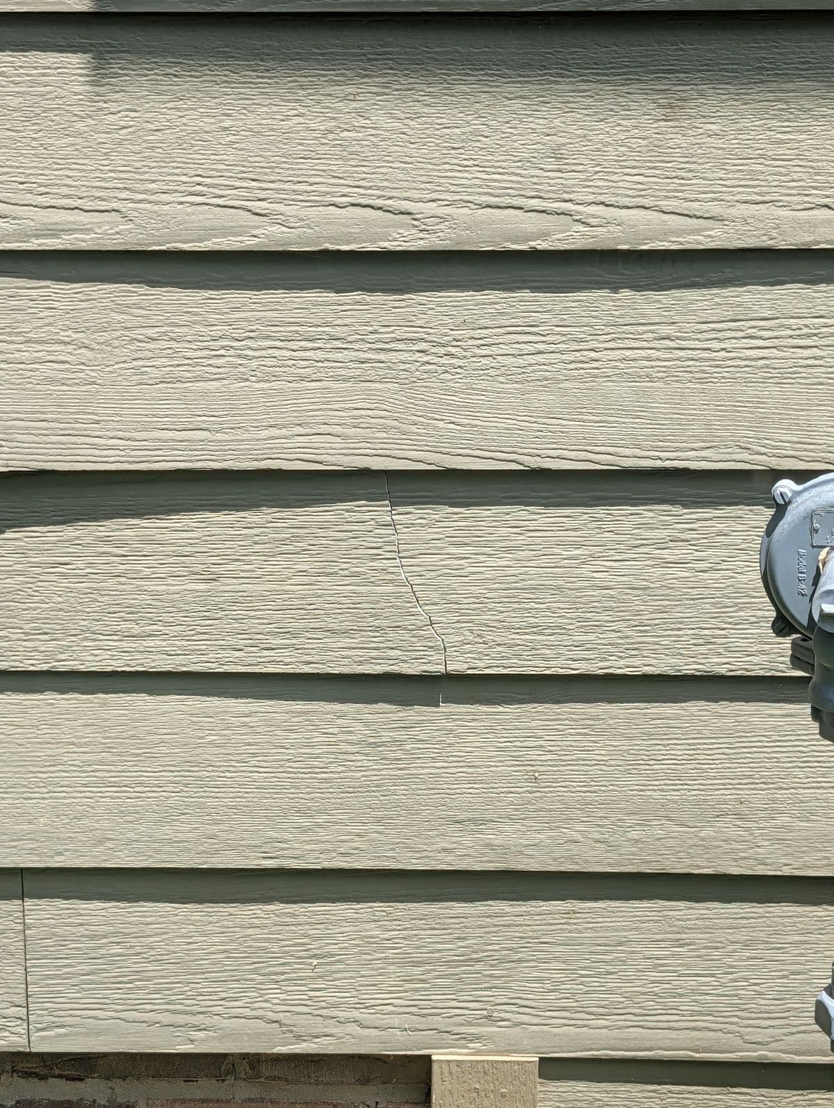 Cracked siding board near the gas meter before repair