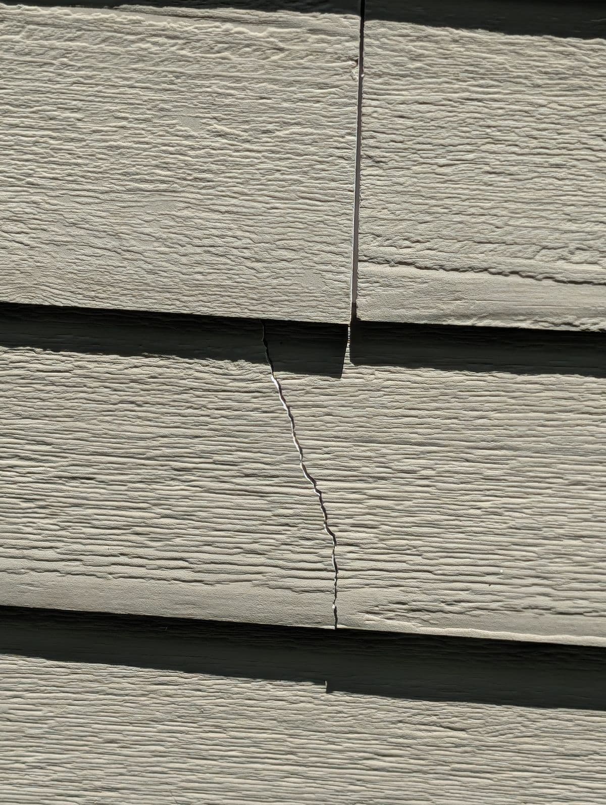 Split fiber-cement siding board with an open gap before repair