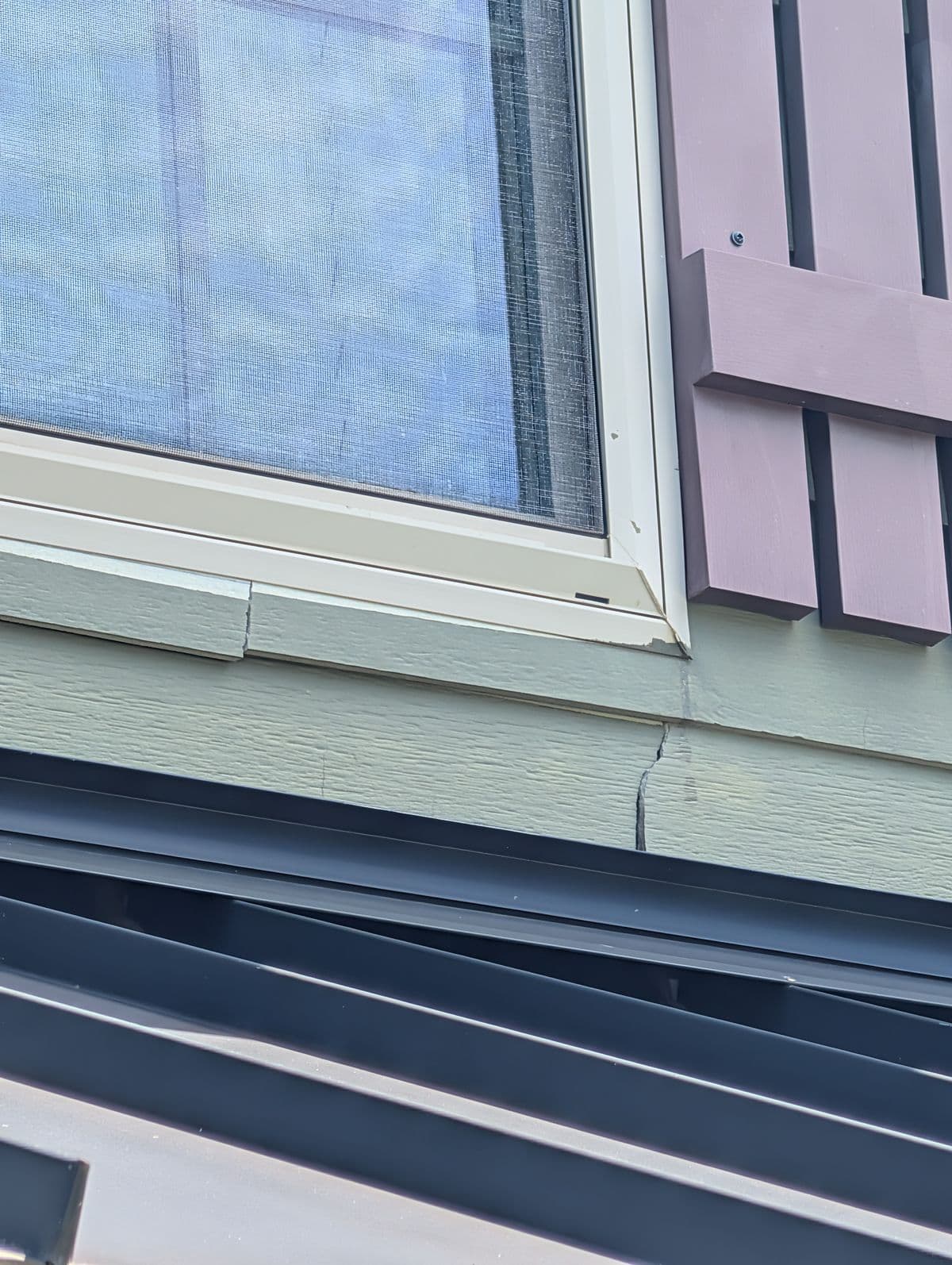 Cracked siding beneath a window with faded shutter before repair