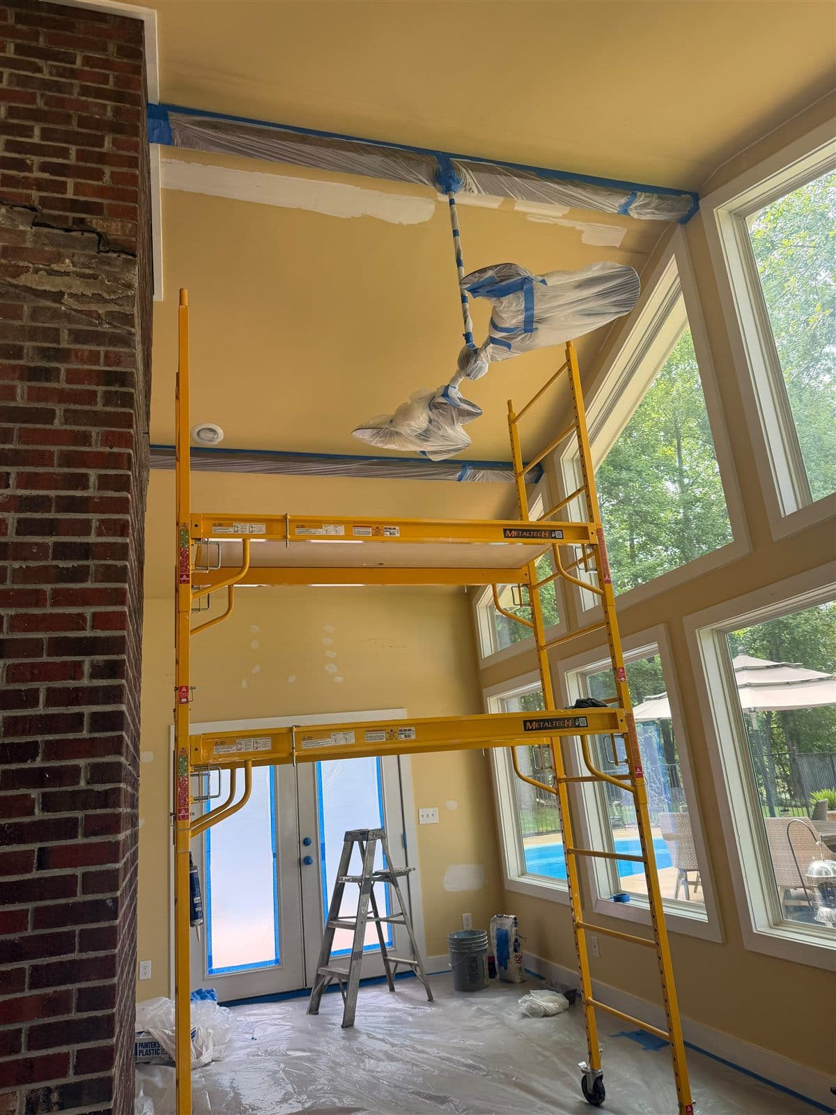 Lake room before painting — old yellow walls, scaffolding, and patched ceiling corners in Pelzer, SC