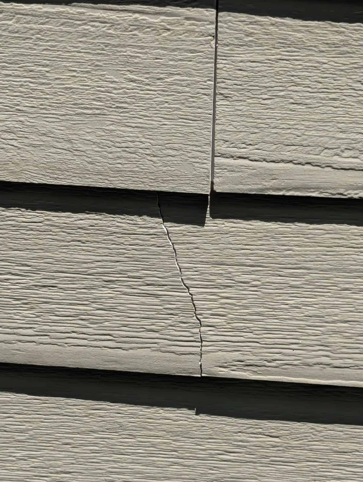 Split fiber-cement siding board with an open gap before repair